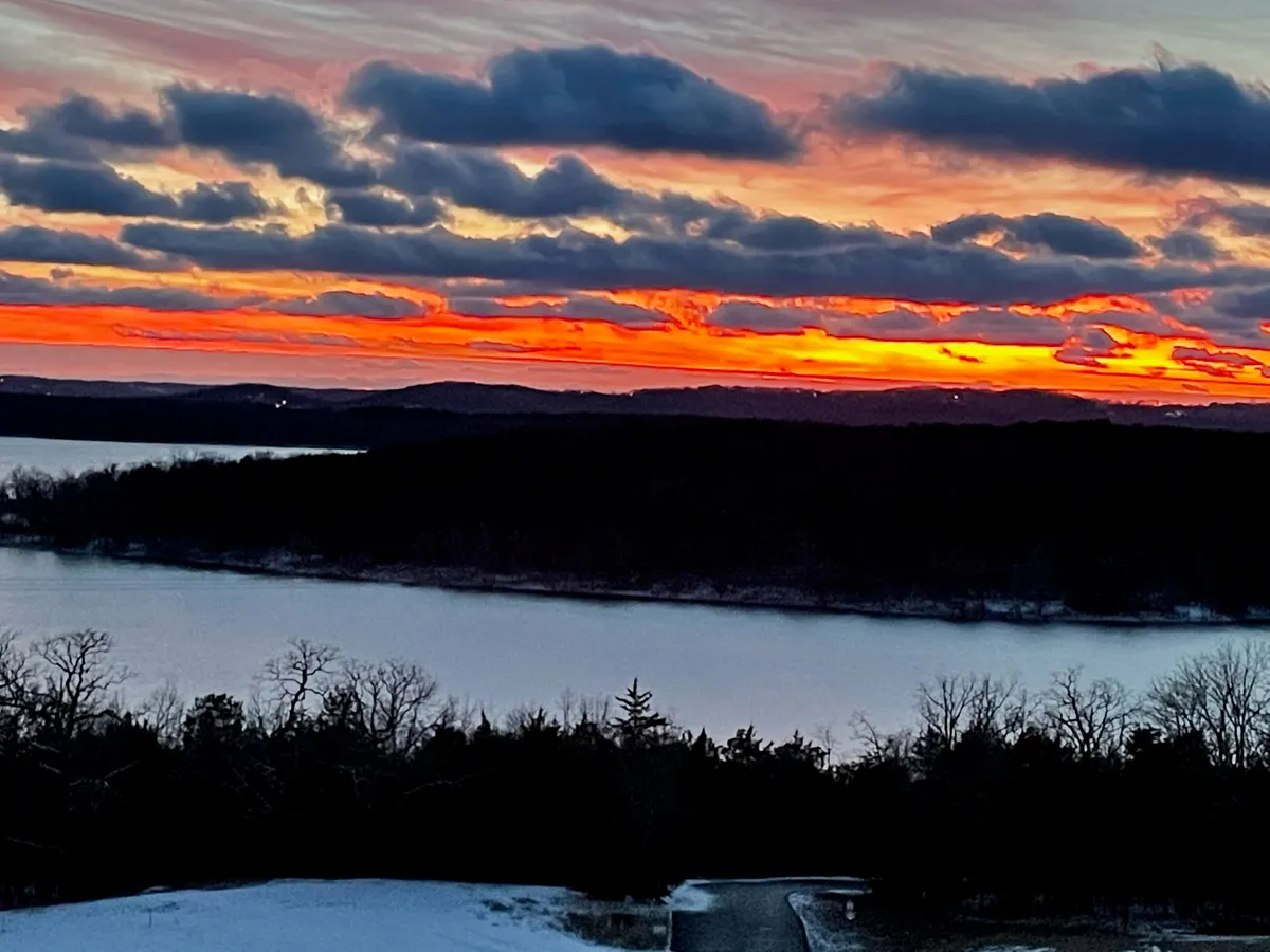 A vibrant sunset over calm Table Rock Lake with distant hills, offering a breathtaking view that evokes serenity and togetherness.