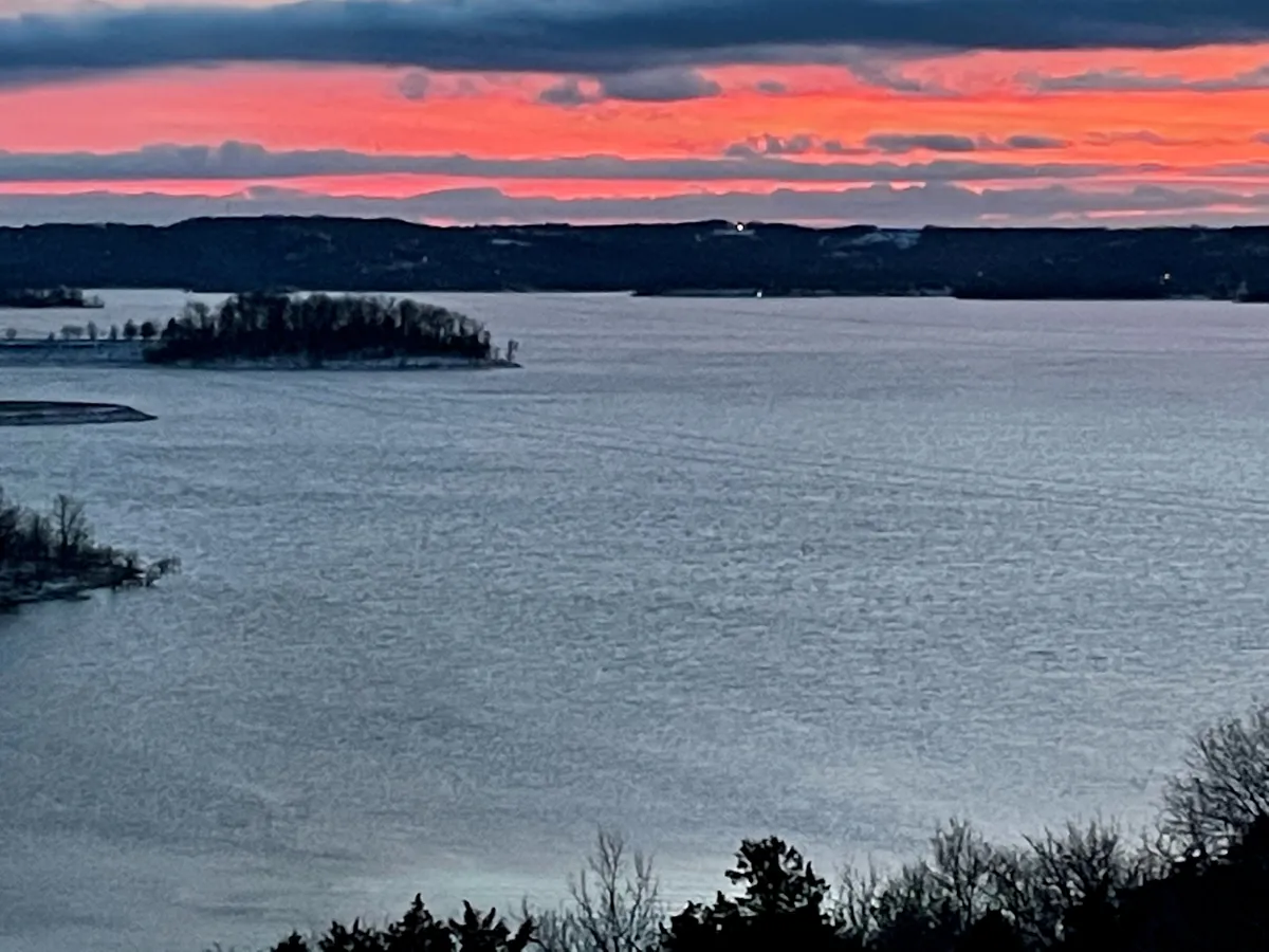 A stunning lake view at sunset, with tranquil waters, distant hills, and a small island. The expansive sky glows with warm evening colors, evoking relaxation and inspiration. Perfect for illustrating the proximity to lake activities and the atmosphere that guests can enjoy during their stay.