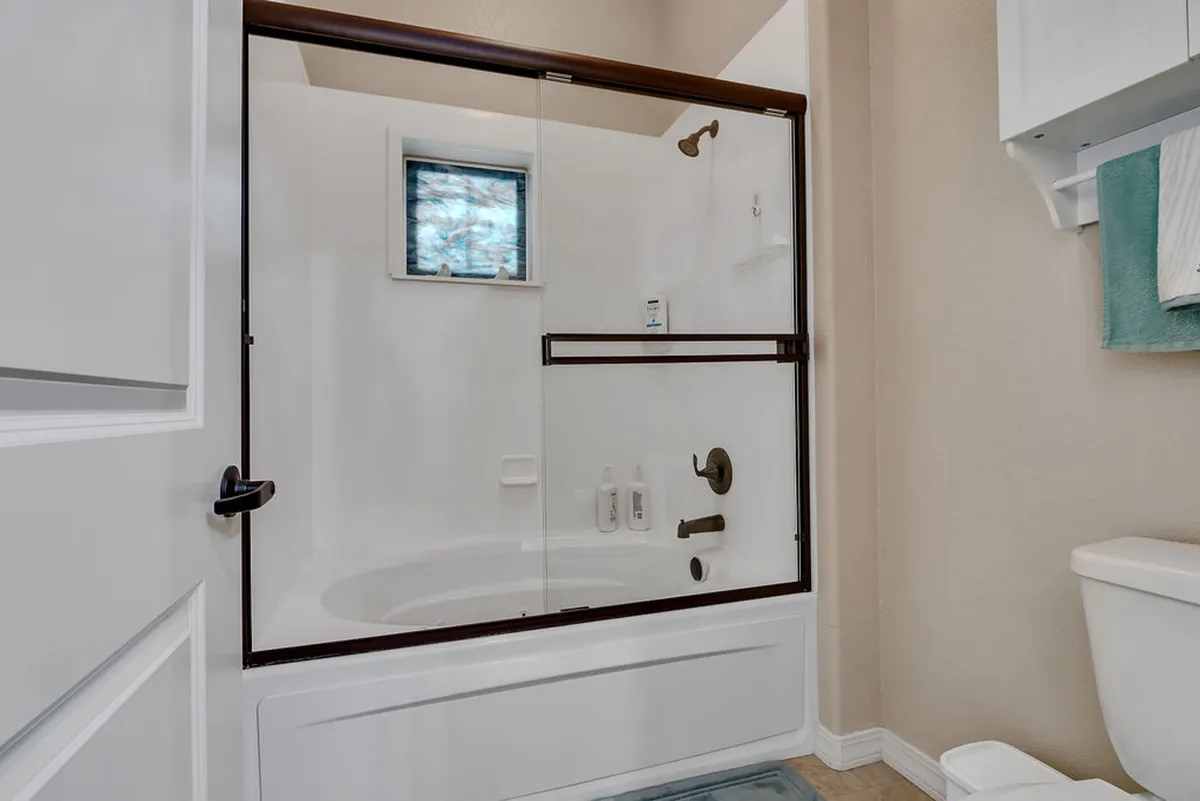 A luxurious bathroom featuring a glass shower enclosure, inviting bathtub, window with patterned glass for privacy and light, and a neatly arranged towel rack. The space feels tranquil and spa-like, ideal for self-care routines and relaxation after a day of adventure.