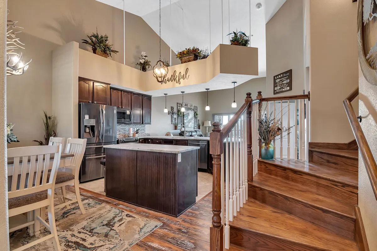 A welcoming view into the open-concept space, featuring a modern kitchen island at the forefront, seamlessly flowing into a spacious dining area. Warm pendant lights illuminate the area, and a staircase hints at the expansive layout. The setting is styled for gatherings and culinary creativity, with ample counter space and inviting seating.
