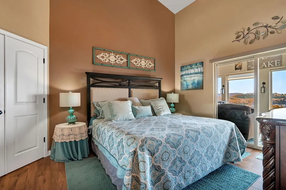 A tranquil king bedroom with a plush bed, elegant decorative bedding, two bedside lamps, and tasteful artwork on the walls. The room exudes calm and offers a cozy, serene space for both relaxation and rejuvenation. The window promises gentle natural light and a peaceful start or end to the day.