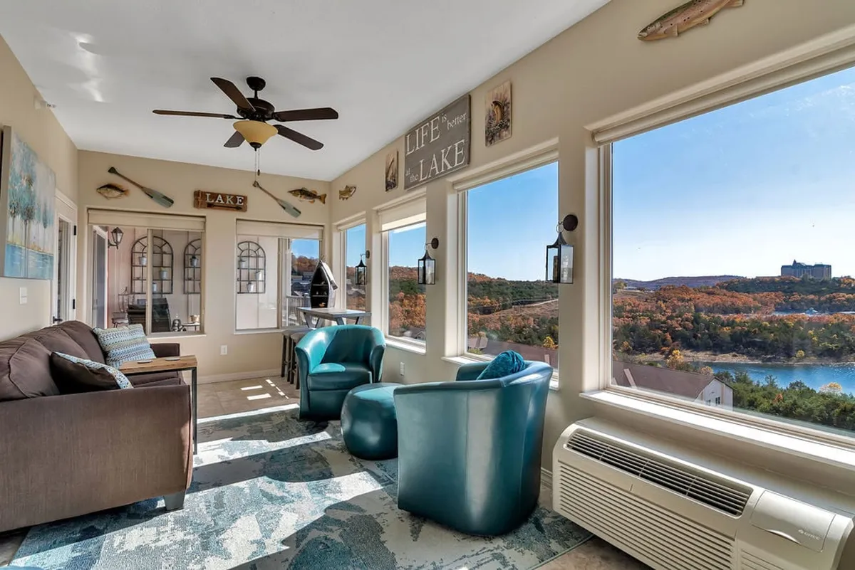 Another sunroom perspective showcasing large windows overlooking the lake, a tranquil seating area, and decorative wall accents. The space is bathed in natural light, offering an inviting environment for morning coffee, reading, or socializing.