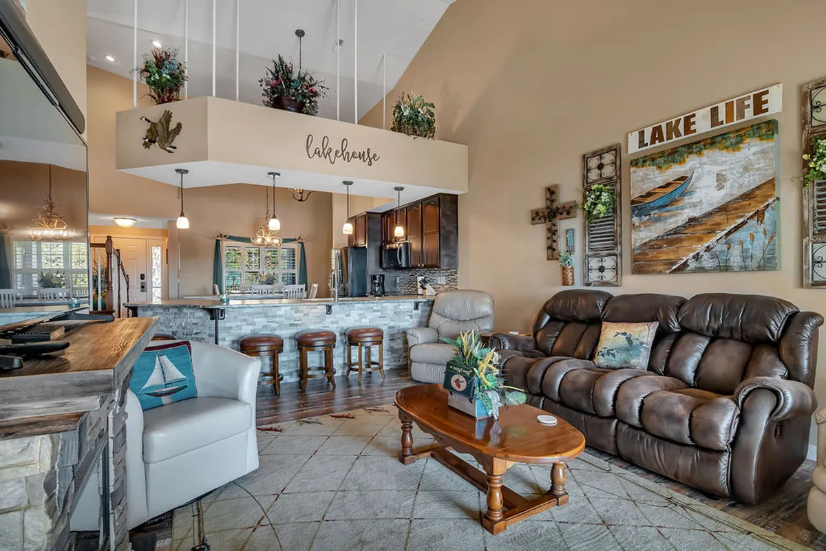 A cozy living room scene with a comfortable leather sofa, lake-themed wall art, and a view of the kitchen bar area in the background. The layout is perfect for relaxing or hosting game nights by the fireplace, capturing the warmth and relaxation described in the section.